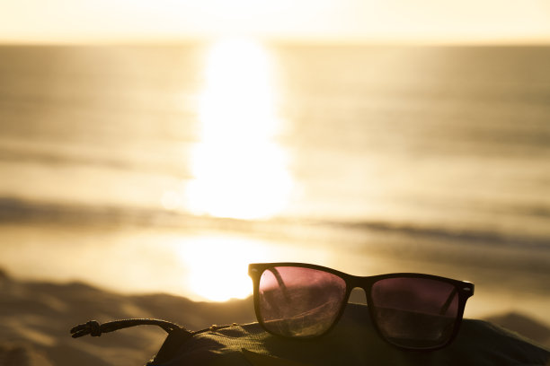 太阳眼镜放在沙滩上，背景是海的地平线，阳光反射在海浪上。图片下载