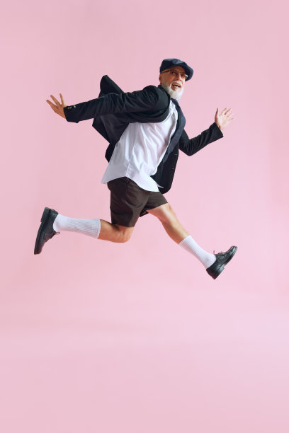 侧面侧面照片的资深大胡子男子穿衬衫黑色短裤漂亮的太阳眼镜兴奋跳跃的空间孤立在柔和的粉红色背景图片下载