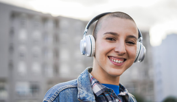 以城市为背景的光头女孩户外听音乐的肖像-城市生活方式概念-主要关注眼睛图片下载