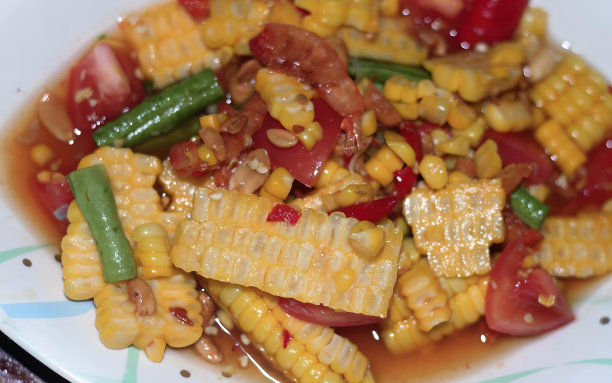 一盘蘸着酱汁的玉米和蔬菜的照片，蘸着酱汁的玉米和蔬菜用勺子放在盘子上。图片下载