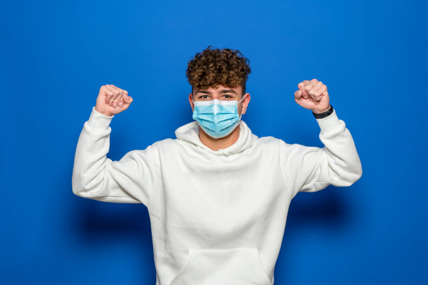 戴着医用口罩、高举双臂站着的白种人的照片显示出了强壮的二头肌。孤立的背景。抗击新冠肺炎保持强壮和健康的理念。图片下载