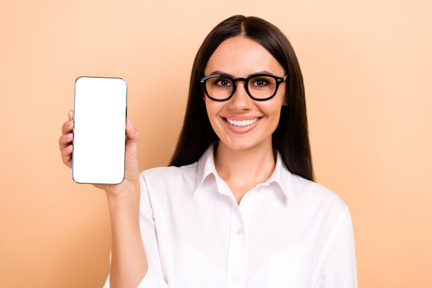 照片的年轻推动者商务女士穿着时尚的衬衫拿着智能手机显示金融应用程序孤立的米色背景图片下载