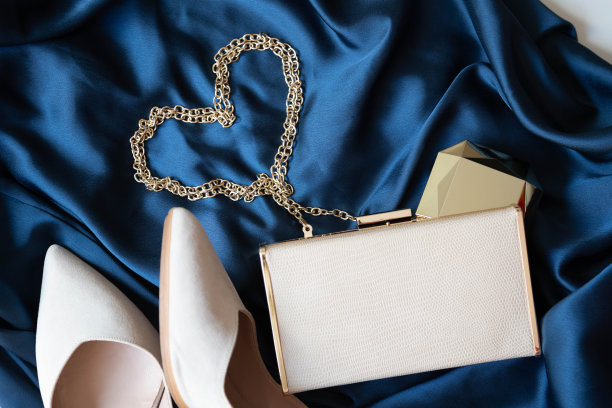 一件鸡尾酒蓝色的连衣裙上挂着一个镶着金链子、金粉和米色高跟鞋的米色女士小手提包。图片下载