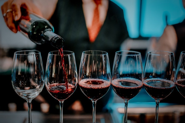 酒吧里的酒保用玻璃杯倒红酒。男侍酒师正在往长柄酒杯里倒红酒。图片下载