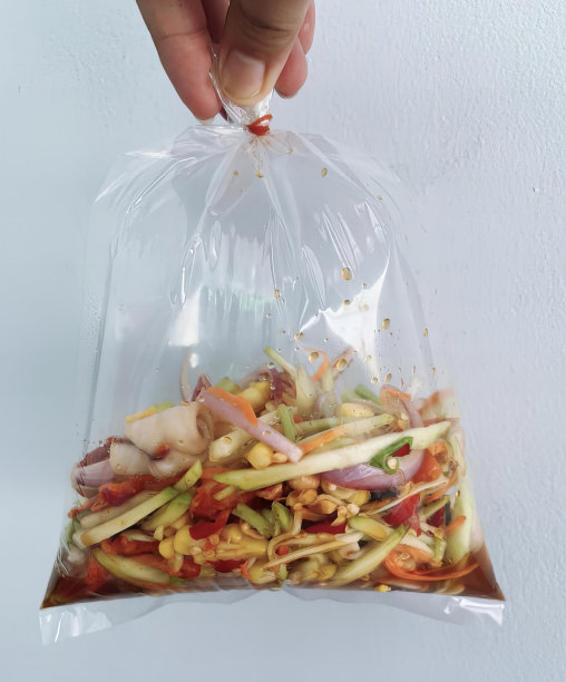 一张照片上，一个人手里拿着一袋食物，桌子上放着装满蔬菜和肉的塑料袋。图片下载