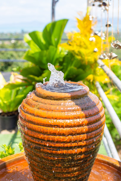 一个带喷泉的水壶，背景是热带的绿色植物。花园中的装饰元素图片下载