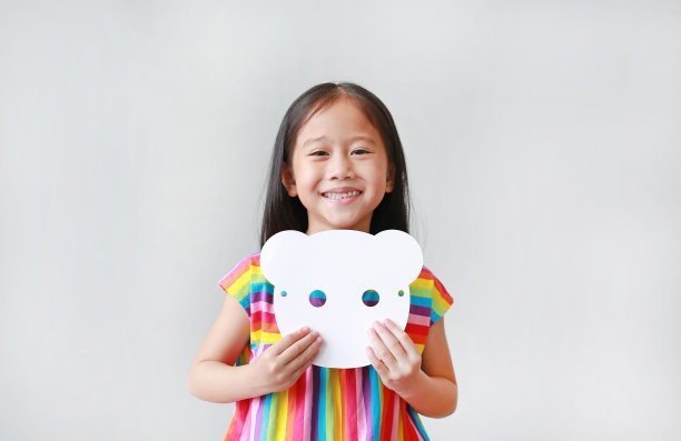 快乐的小女孩抱着空白的白色动物纸面具在她的胸部在白色的背景。孩子装扮成动物脸的想法和概念。图片下载