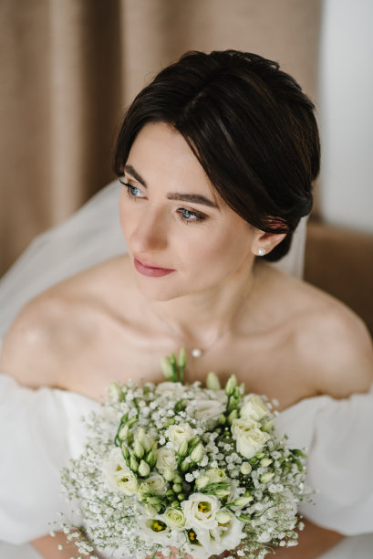 年轻的时尚模特，完美的皮肤和专业的化妆。新娘穿着时髦的礼服坐在家里的沙发上。奢华的婚礼。时尚照片。等待新郎。时尚的婚礼风格照片。图片下载