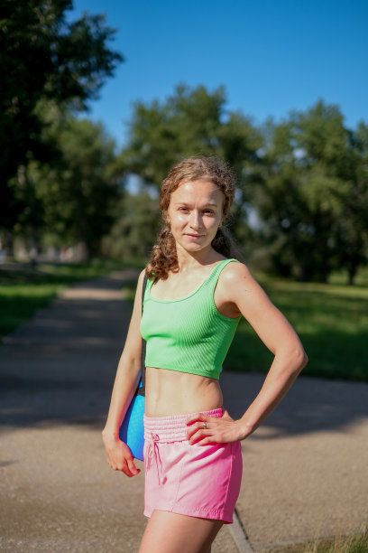 在公园里，一个年轻的卷发女人从后面拿着瑜伽垫和健身服的照片。图片下载