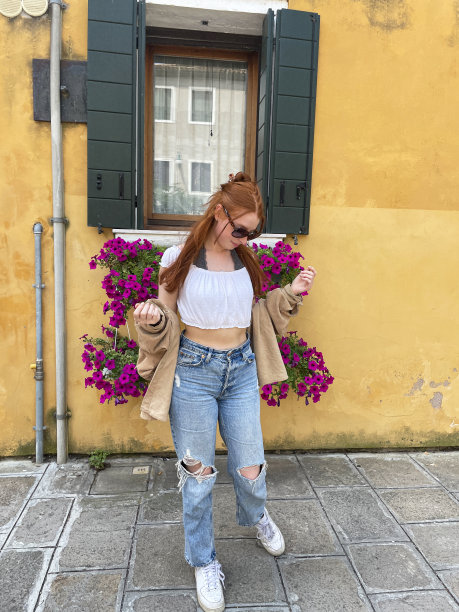 特写照片，迷人的红发女人戴着墨镜，走在意大利威尼斯布拉诺的小巷里，欣赏色彩缤纷的建筑物和建筑，聚焦在前景上图片下载