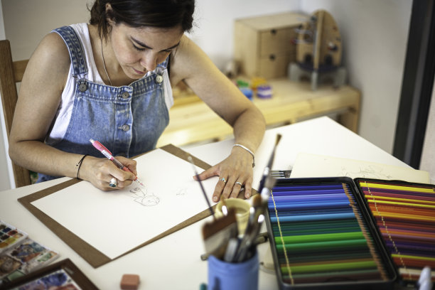 插图画家在她的家庭工作室桌子上工作，所有的材料。彩色铅笔、画笔和水彩画。图片下载