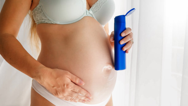 穿着内衣和内裤的孕妇在身上涂抹面霜，照顾她的皮肤。美容、怀孕、护肤的理念。图片下载