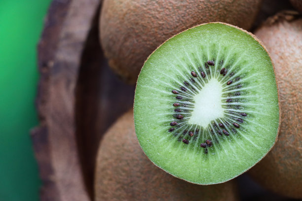 全画幅图片，一堆猕猴桃(猕猴桃)在木制果盘里，中国醋栗切成两半，显示模糊的棕色皮肤和亮绿色的果肉，黑色的种子环，斑驳的绿色背景，高架视图图片下载