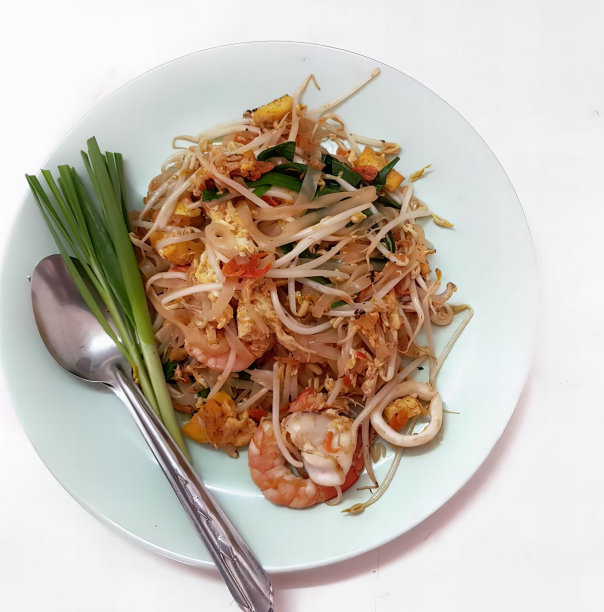 一盘有勺子和叉子的食物的照片，一盘有虾、面条和蔬菜的食物放在一张白色的桌子上。图片下载