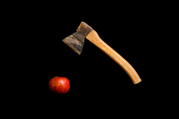 生锈的旧斧头挂在黑色背景上的红苹果上图片下载