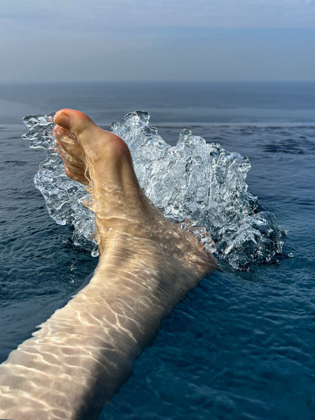 特写照片:无法辨认的男子的脚和脚趾，在无边泳池中溅起的毛茸茸的腿和脚踝，水尾流，坐在泳池边的白人男子的脚漂浮在水面上，高架视图图片下载