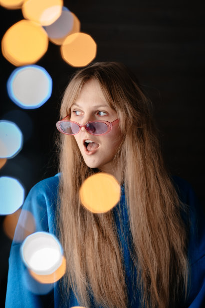 一个戴粉红色眼镜的女孩。一个穿蓝色连帽衫的女人。有灯光效果的照片图片下载