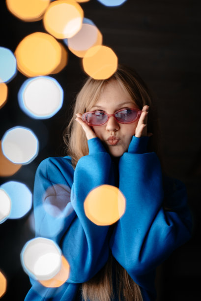 一个戴粉红色眼镜的女孩。一个穿蓝色连帽衫的女人。有灯光效果的照片图片下载