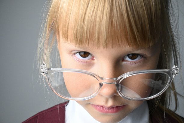 一个棕色眼睛戴着大眼镜的小女生的微距肖像。灰色的背景。从眉毛下面看。图片下载