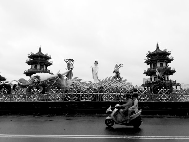 高雄,台湾。2019年8月20日，台湾阴雨天气，一辆摩托车从一座古代历史雕塑(龙、观音)的黑白照片中驶过。宝塔)。图片下载