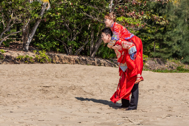 这是一对美丽的情侣在黄色的沙滩上的照片，中国的新婚夫妇穿着鲜艳的红色民族服装图片下载
