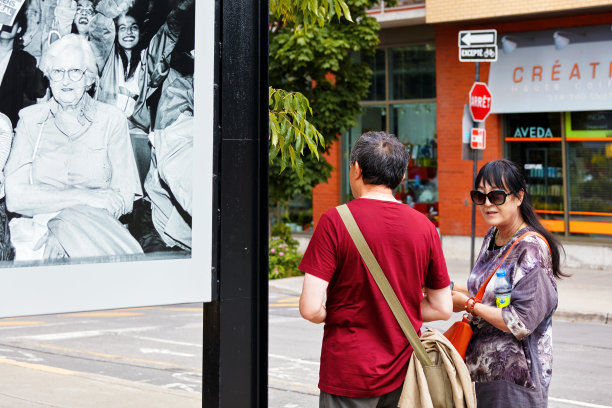 一对中年亚洲夫妇走在街上，旁边的广告牌上有一位年迈的加拿大妇女的照片图片下载