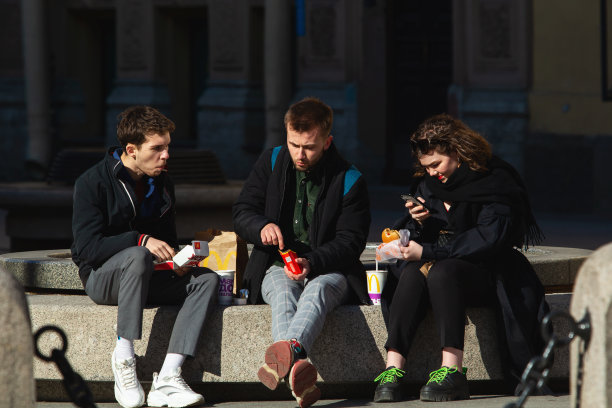 一群人坐在大理石长凳上吃快餐的侧视图。两个男孩和女孩正在吃汉堡包图片下载