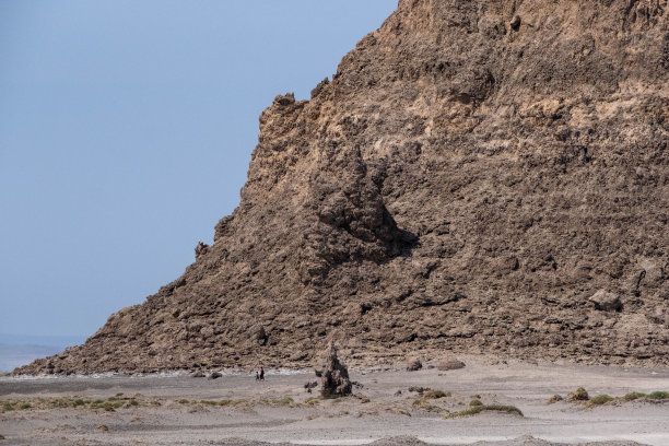 两个孩子走在阿贝湖盐碱地沙漠的一个岩层旁边图片下载