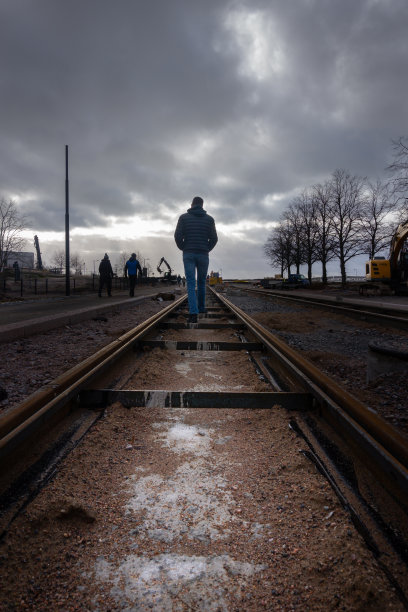在欧洲芬兰赫尔辛基，一个阴天里，一名身穿夹克的年轻白人男子在铁路上行走图片下载