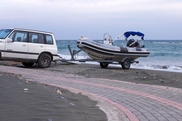 一辆白色吉普车拖着一只充气橡胶船在海边。图片下载