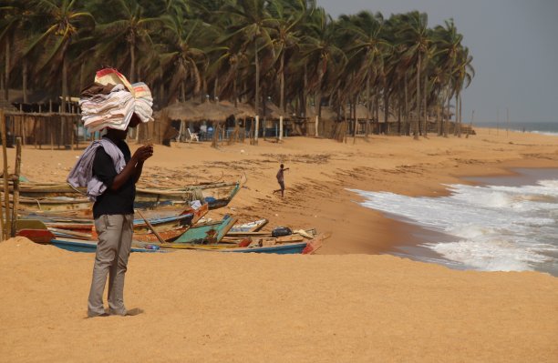 西非多哥阿韦波佐海滩上，一名海滩小贩头上顶着织物。图片下载
