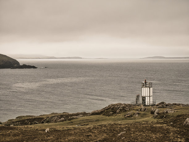 英国设得兰群岛Muckle Roe的舌头山下的遥控自动化太阳能灯塔，背景是Minn的Swarbacks图片下载