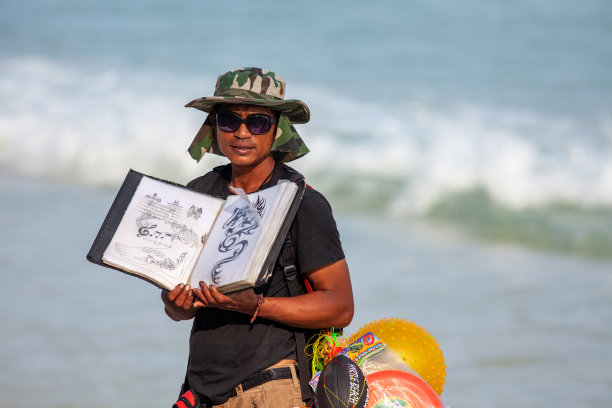 泰国苏梅岛——2011年1月9日:在苏梅岛的查翁海滩上，一位泰国商人向游客展示纹身样品图片下载