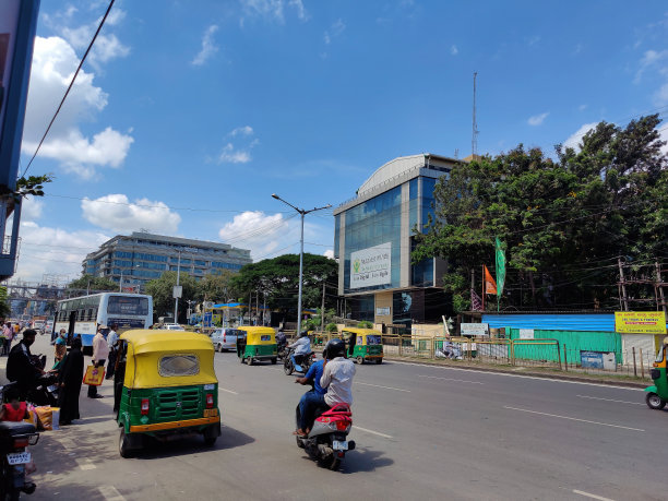 在明亮的下午，在班加罗尔主干道周围的多层公司大楼里，人们在crawdad路上乘坐车辆，等待公共汽车的股票照片。图片下载