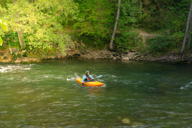 穿着救生衣和头盔的男子在河里练习划皮划艇图片下载