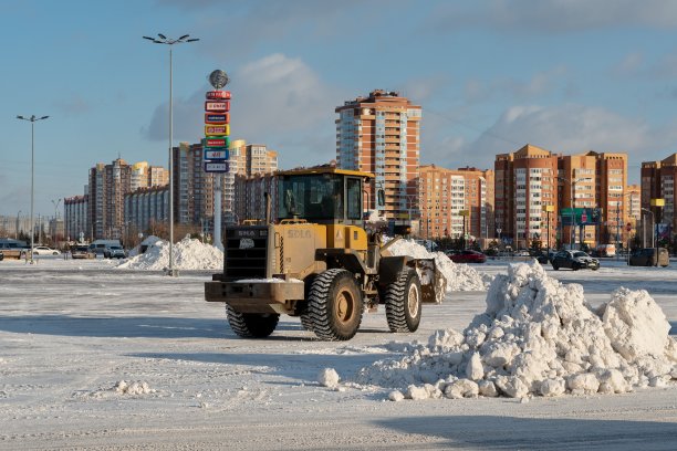 在一个阳光明媚的日子里，一场降雪后，一辆铲斗铲运机从城市广场的雪堆中清除积雪。图片下载