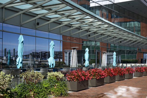 玻璃幕墙建筑旁边的路边咖啡馆，有加热灯和雨伞。盆栽红花作装饰图片下载