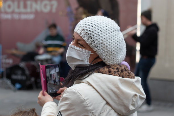 爱尔兰，都柏林，亨利街，一个戴着白色帽子，戴着面具的快乐的成年妇女正在拍摄街头音乐家的照片图片下载
