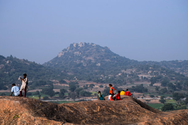 少数人或游客坐在山顶欣赏风景的照片，在明亮的阳光下拍摄的背景山脉。图片下载