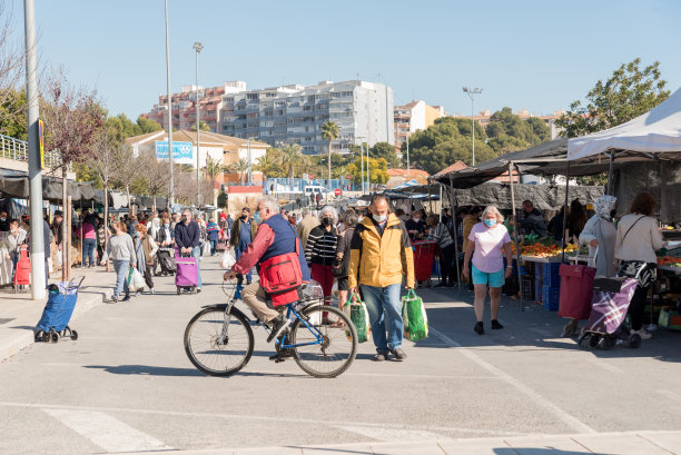 水果和蔬菜街头市场有很多人购物，一个人骑自行车，人们拿着袋子和手推车。图片下载