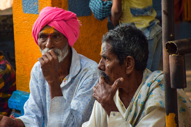 在寺庙举行神圣仪式时，一位印度老人或男子穿着白色衬衫和粉红色头巾，坐在寺庙楼梯上的照片。模糊的背景图片下载
