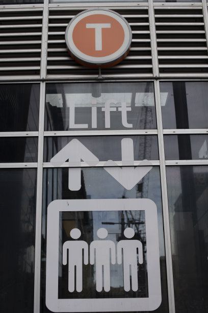 电梯到达玻璃幕墙的马丁广场火车站。建筑物和起重机反射在玻璃上。图标显示三个人和箭头。图片下载