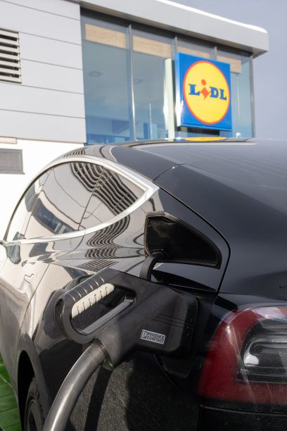 这是一张静态照片，拍摄的是在一个阳光明媚的冬日里，一辆黑色特斯拉Model 3双电机在LIDL超市的直流充电站充电。有选择性的重点图片下载