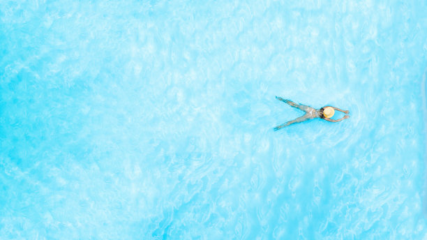 身穿比基尼和帽子的年轻美女独自在游泳池里游泳。无人机从上面拍摄的照片。热带的暑假图片下载