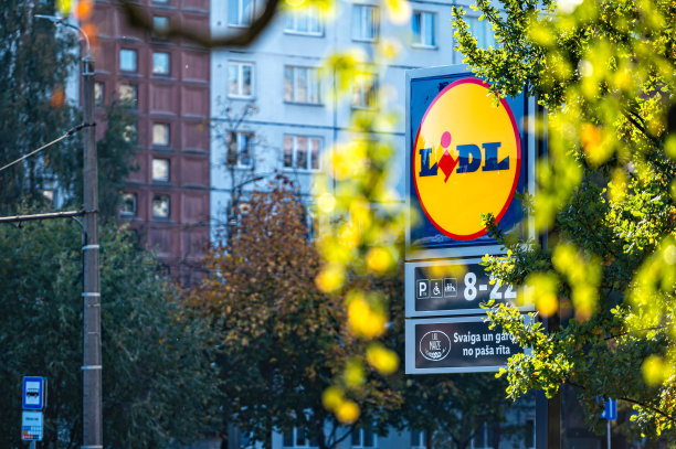 站在LIDL连锁超市的标志通过散焦的秋天树的树枝图片下载