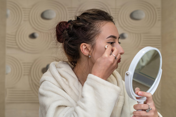 浴室里，一个年轻漂亮的女孩正对着镜子打粉底。图片下载