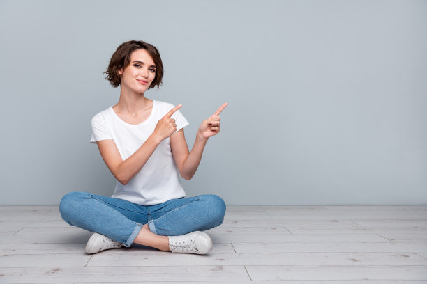 穿着白色t恤的漂亮漂亮的女人的全尺寸照片坐在地板上，在灰色背景上提供孤立的空白空间图片下载