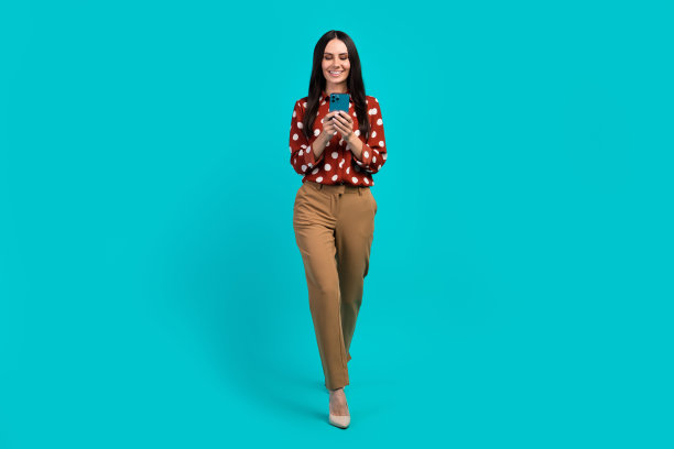 经典的正面漂亮女孩的全尺寸照片走路用智能手机写博客帖子孤立的蓝绿色背景图片下载