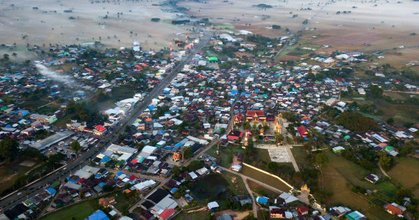 从空中俯瞰美丽的绿色稻田和村庄的无人机航拍照片。这条路穿过小村庄，通向绿色的稻田。泰国东北部的老房子。图片下载