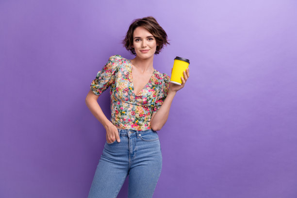 迷人的年轻女子的照片肖像拿着纸杯咖啡穿着时髦的印花衣服孤立的紫罗兰色背景图片下载